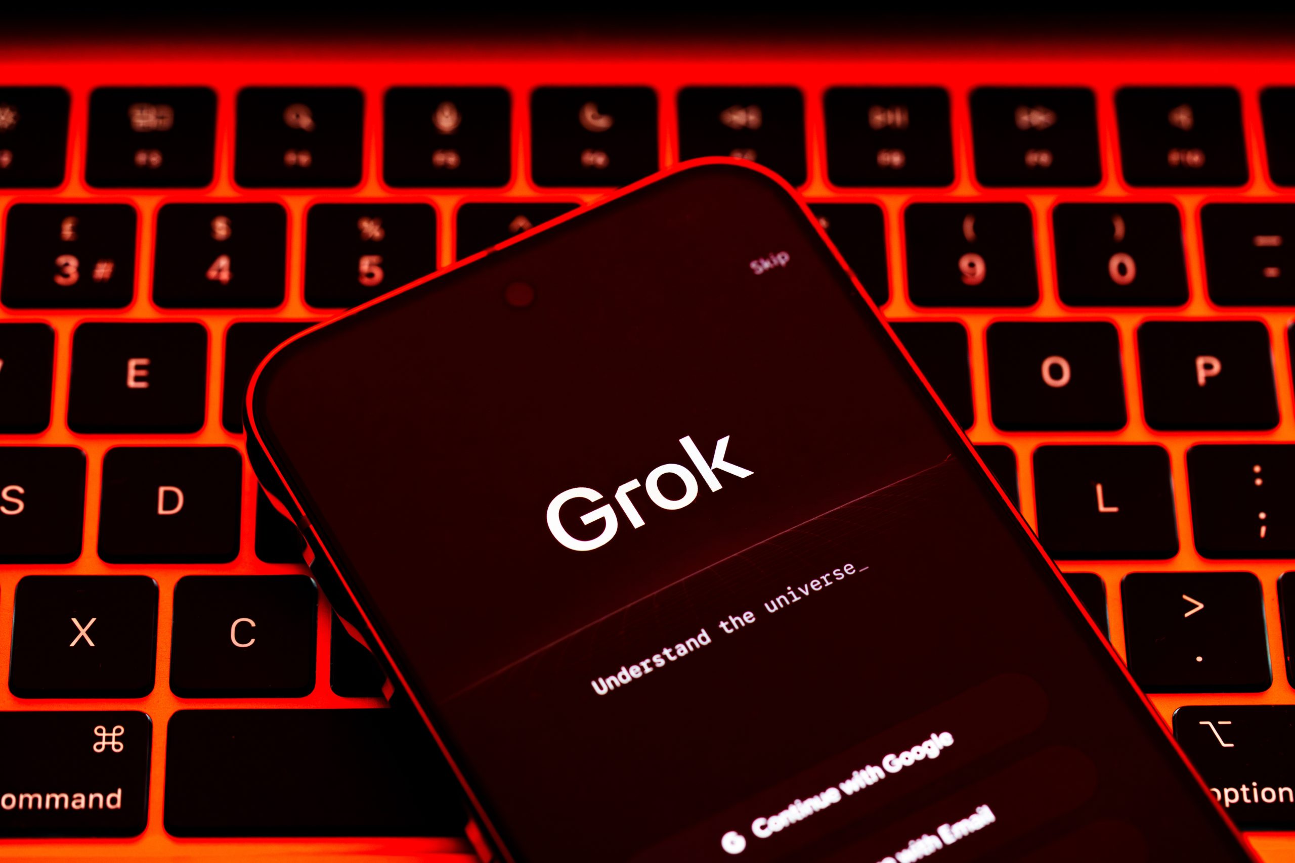 A phone with text "Grok" on top of a laptop keyboard